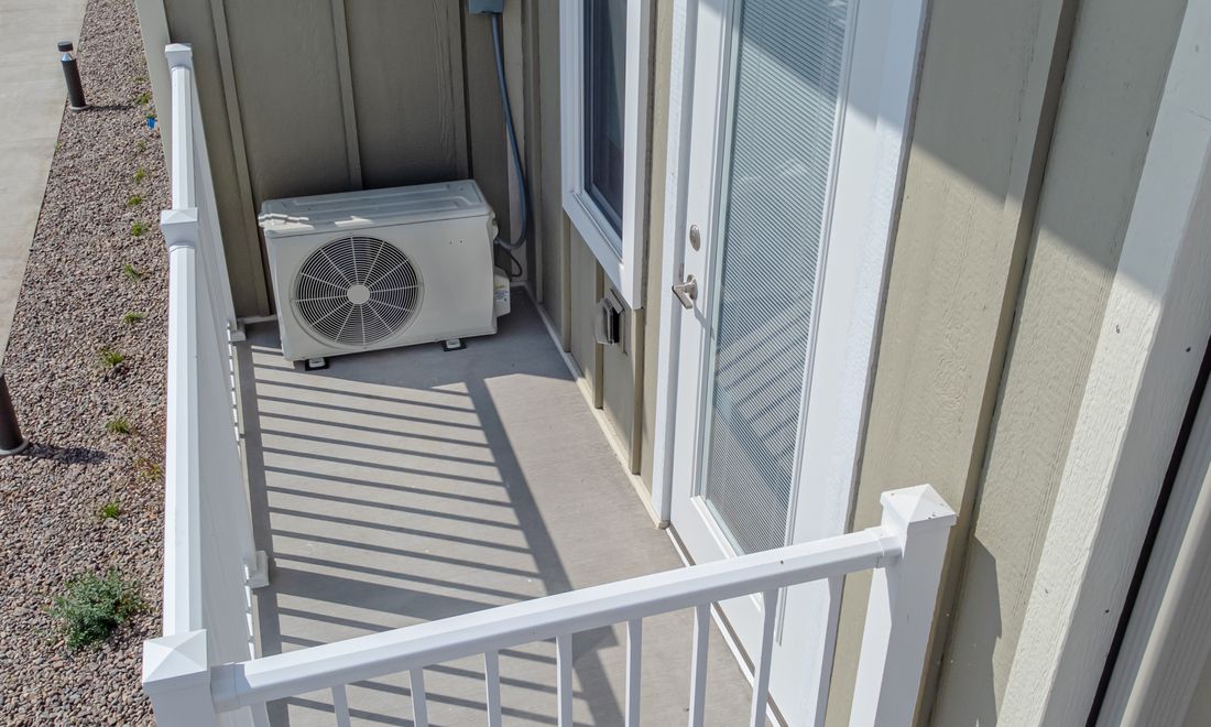 The outdoor unit of a ductless mini-split on a balcony, with its disconnect on the wall